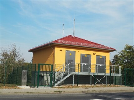 Gelbes Haus mit drei Stahltüren, davor eine Metalltreppe, alles mit einem grünen Zaun abgesperrt