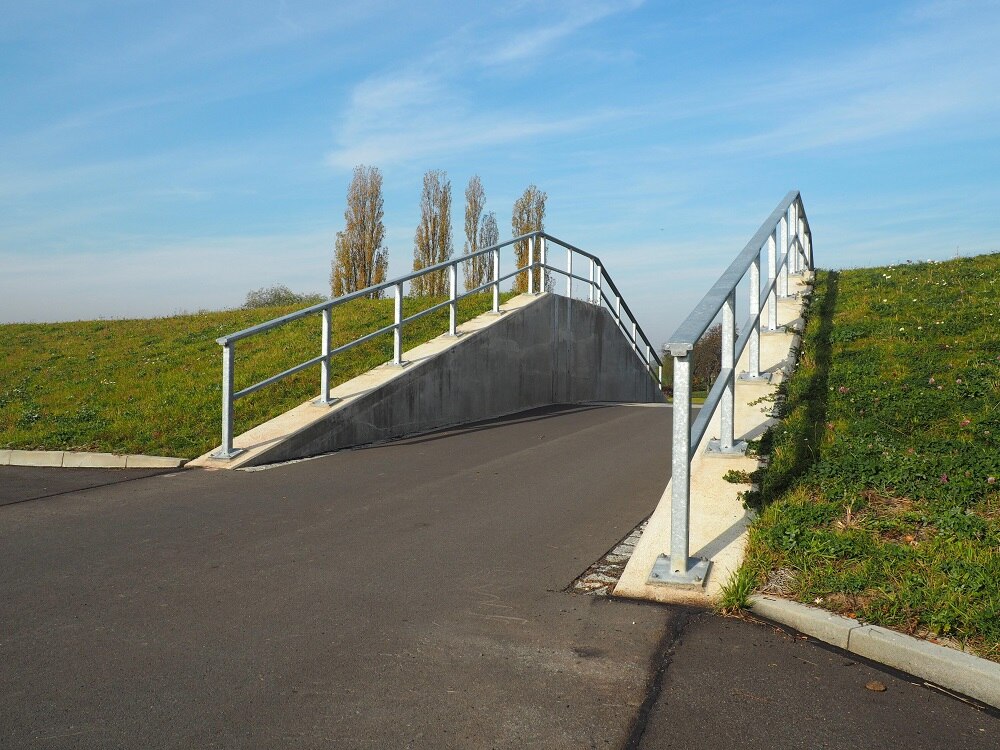 Blick auf eine asphaltierte Straße, die durch einen Deich führt. Rechts und links Geländer