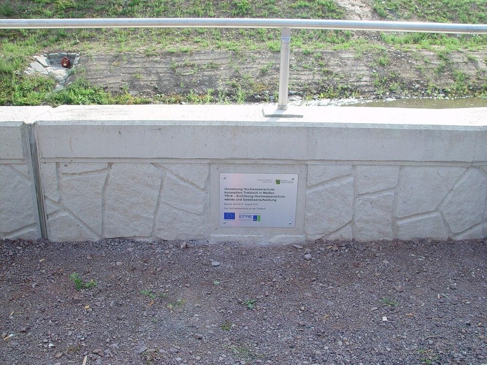 in Boden eingelassene niedrige Mauer mit Plakette mit Informationen zur EU-Förderung