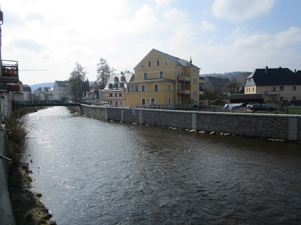 Ein Fluss mit einer Mauer im Hintergrund, dahinter Häuser