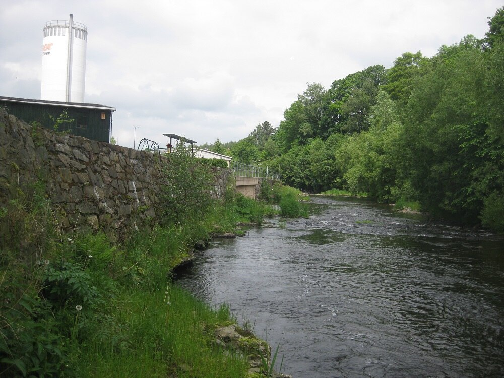 Fluss, der rechts von einer Mauer fließt und Bäume und ein Turm im Hintergrund
