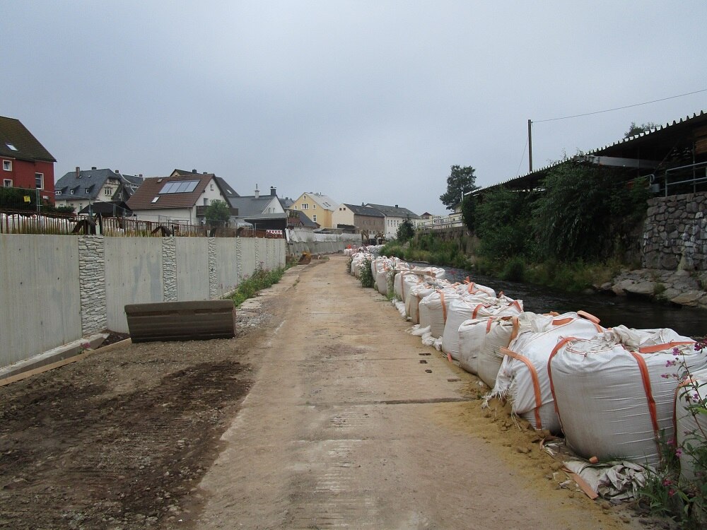 Weg mit weißen Säcken voll Material rechts davon und links eine Betonmauer