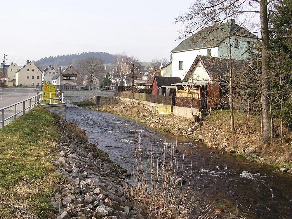 Blick auf einen Fluss, daneben steht ein Haus