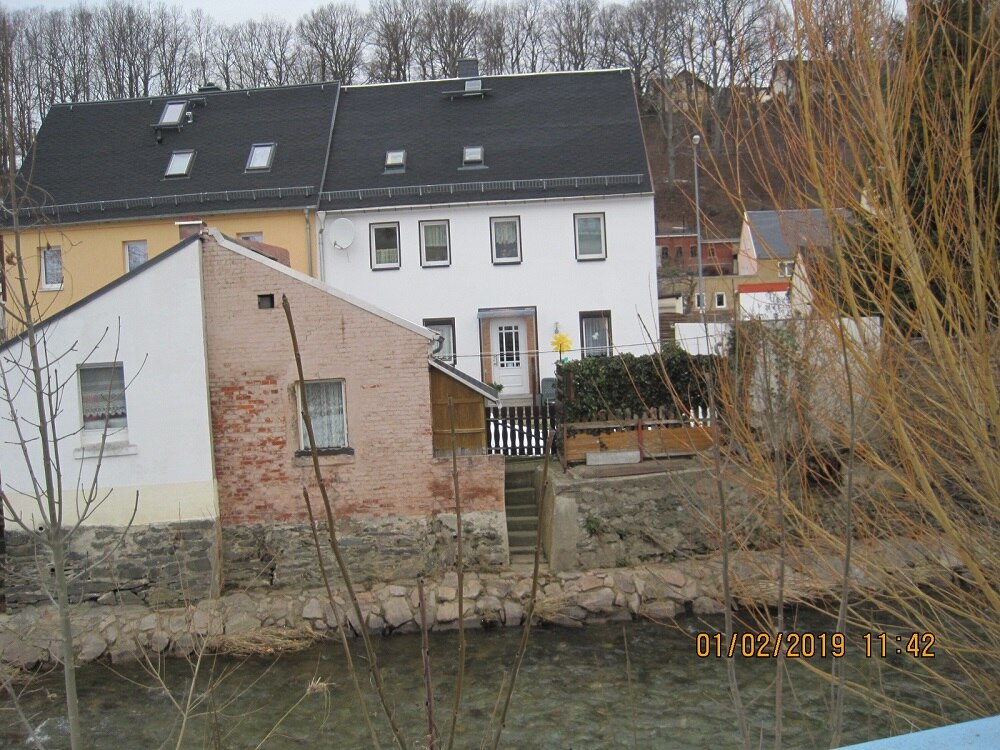 Blick auf vier Häuser, davor ein Fluss
