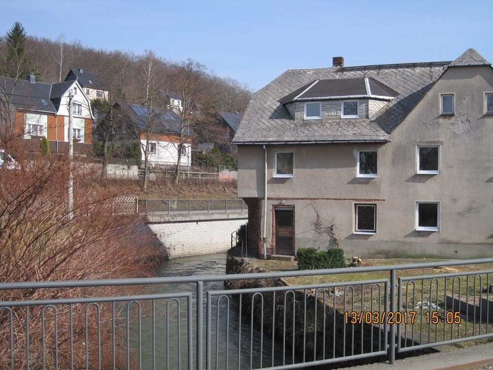 Blick von einer Brücke über einen Fluss auf ein altes Haus, das direkt am Fluss steht