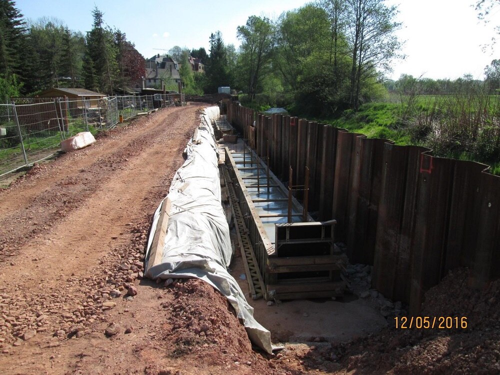 Schotterweg, rechts daneben Metallwand im Boden und Schalung für Bauwerk