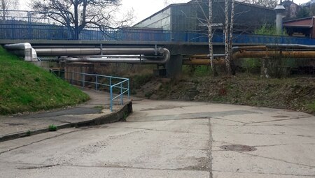 Betonierte Straße mit einer blauen Brücke und Häusern im Hintergrund