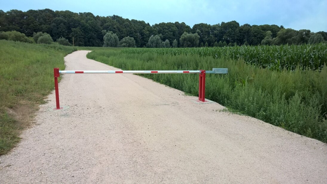 rot-weiße Schranke auf Straße, rechts und links grünes Feld