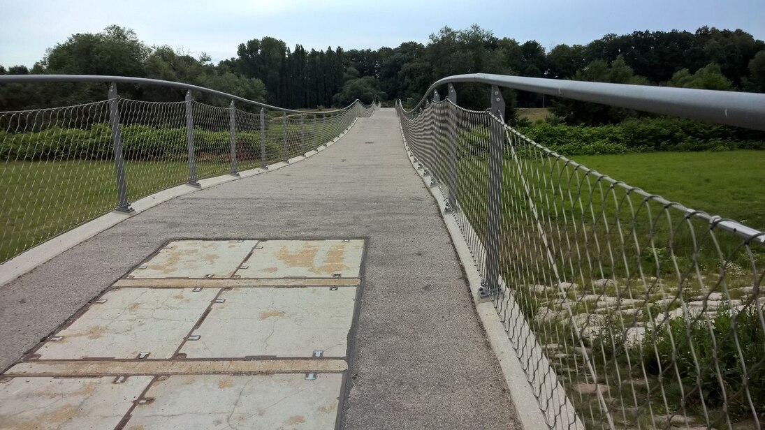 Blick auf eine Brücke mit Metallgitter, dahinter grün