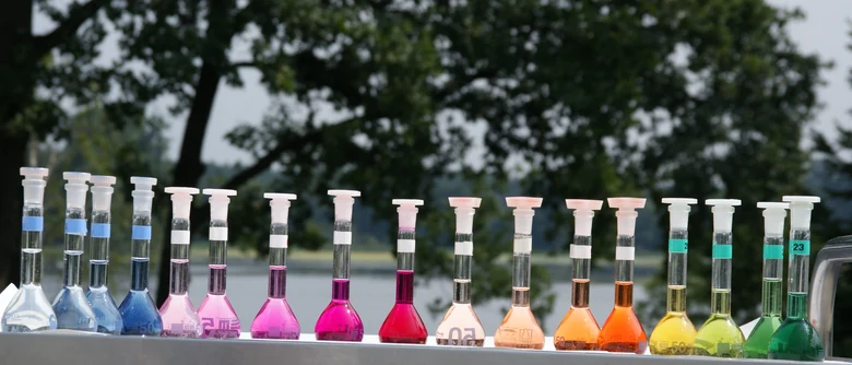 viele Reagenzgläser stehen aufgereiht nebeneinander. In jedem befindet sich eine anders eingefärbte Flüssigkeit. Das Gesamtbild ergibt die Farben des Regenbogens