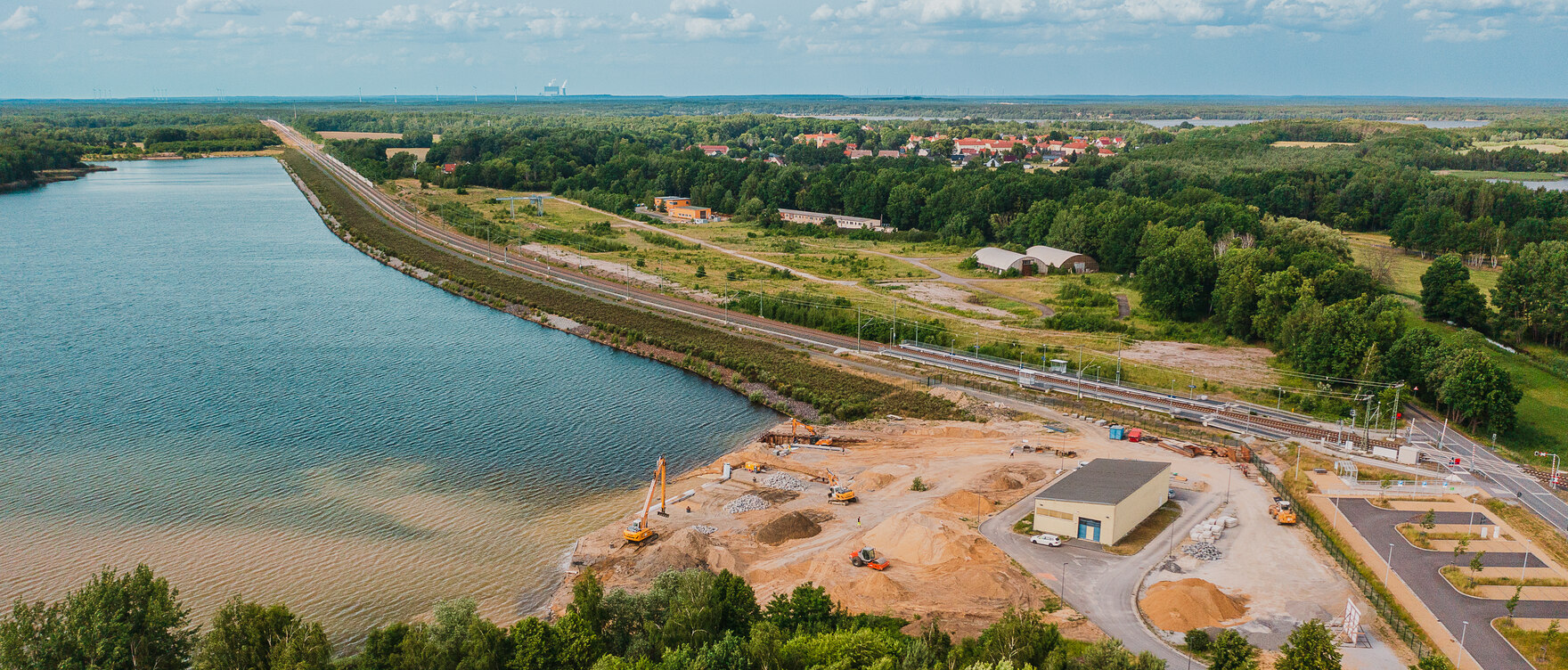 Luftbild von der Baustelle an See und Ufer mit Bagger, Krahn und anderen Baumaschinen 