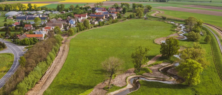 Luftbild auf kurvigen Flusslauf auf der rechten und eine Ortschaft auf der linken Seite