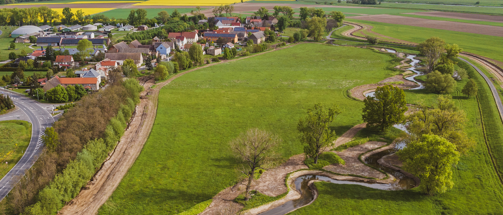 Luftbild auf kurvigen Flusslauf auf der rechten und eine Ortschaft auf der linken Seite