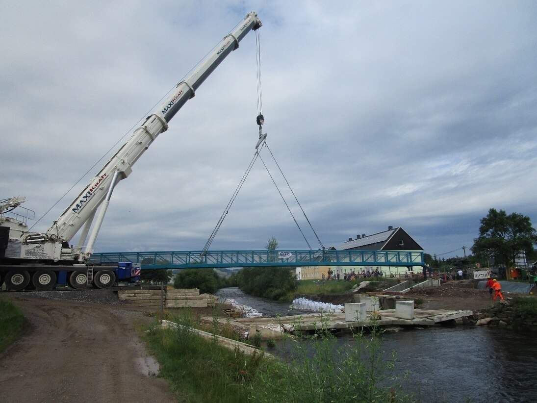 Ein Kran balanciert ein Brückenteil über einen Fluss