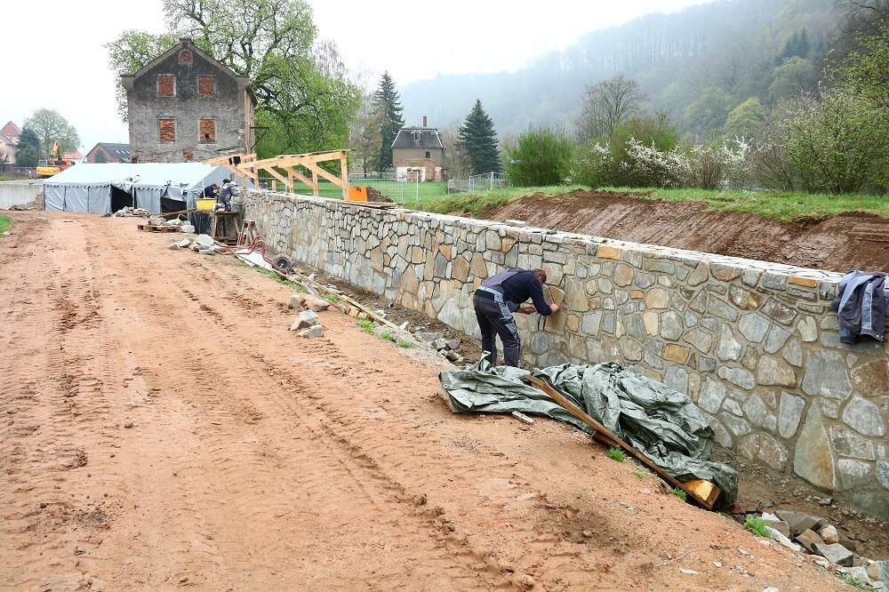 Natursteinmauer im Bau, dahinter Haus