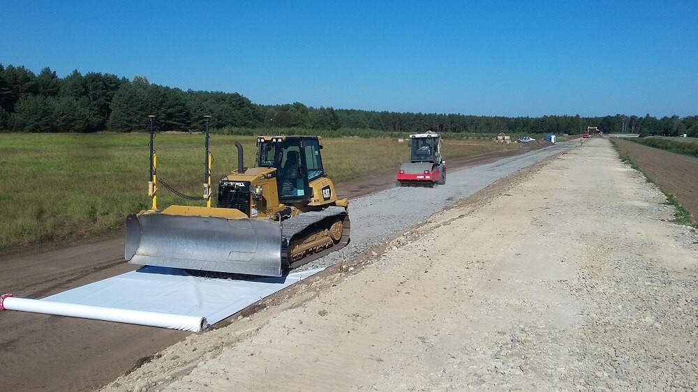 Baustelle mit gelben Raupenfahrzeug und einem kleineren roten Baufahrzeug