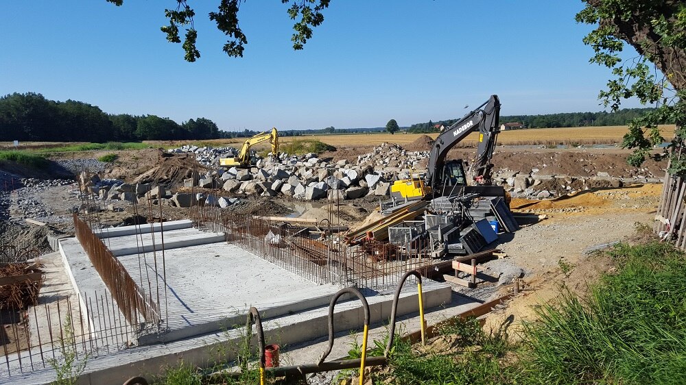 Blick auf eine Baustelle mit Baggern, großen Steinhaufen und einer Betonplatte