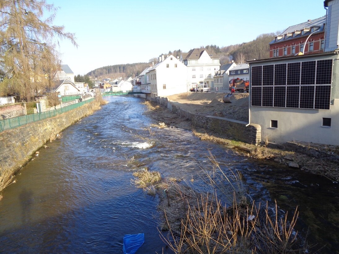 Blick auf Fluss mit Häuserreihe rechts und einer Baulücke