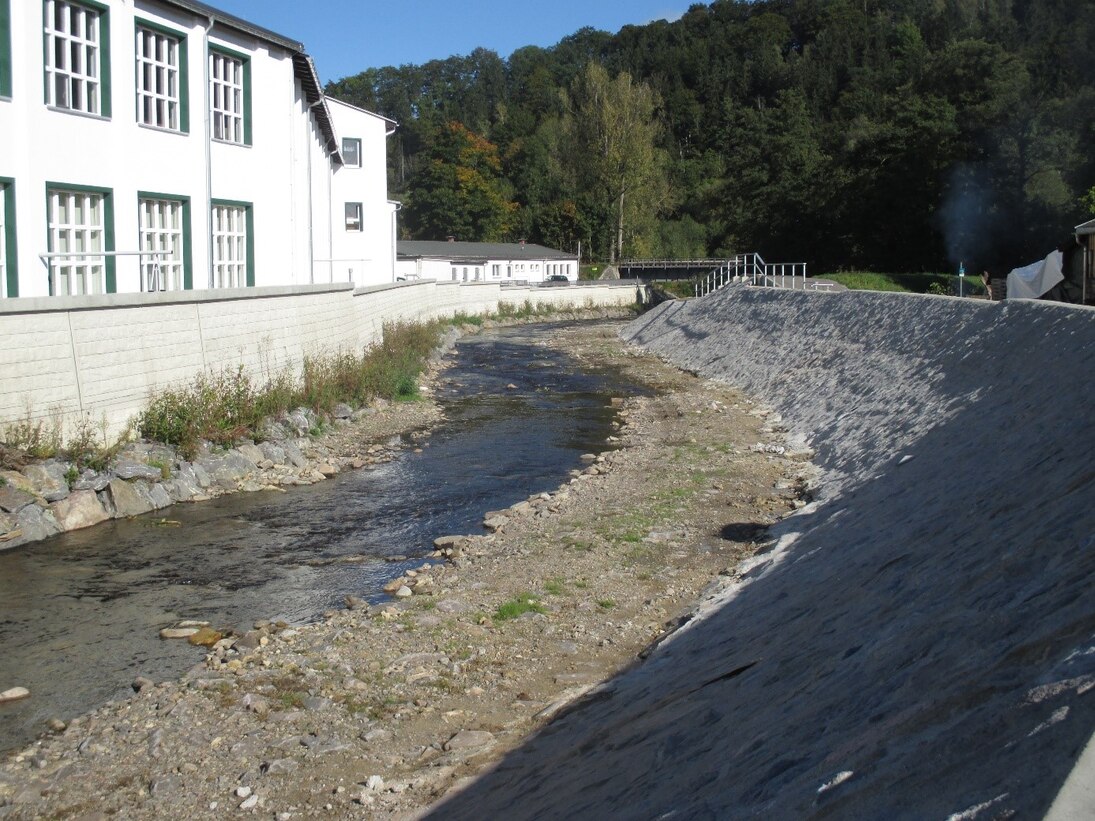 Bild auf einen Fluss vor einem Haus mit Hochwasserschutzwand, der eine Kurve macht