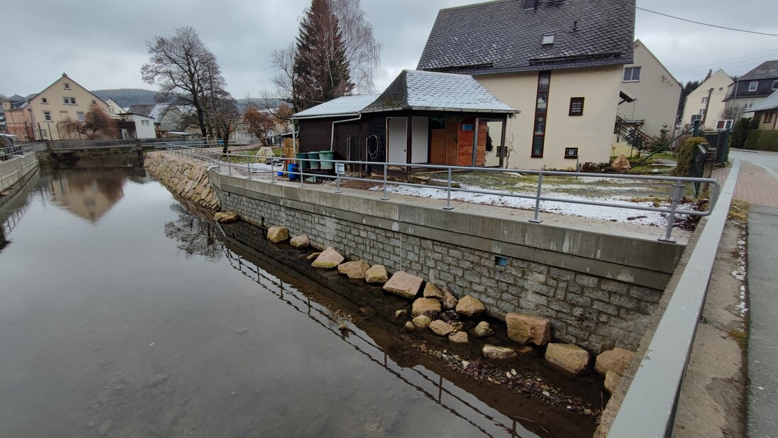 Blick von Brücke auf Haus, davor ein Fluss