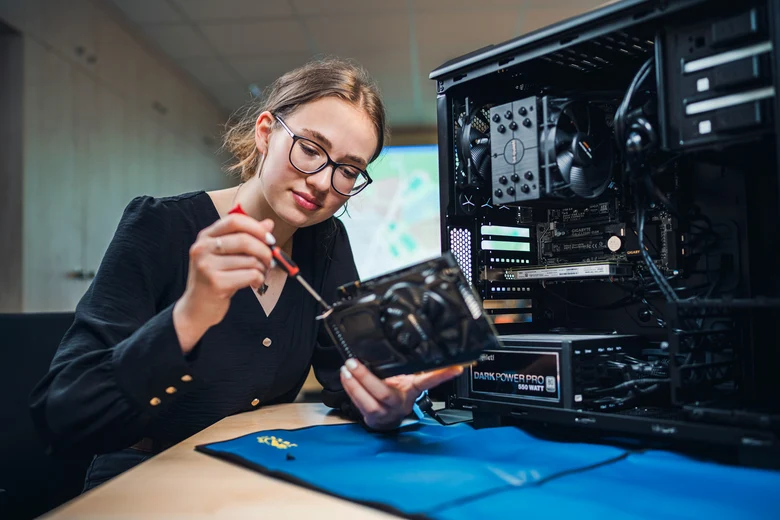 eine junge Frau schraubt mit Schraubendreher an einem Teil eines neben ihr stehenden offenen Computers