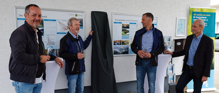 vier Männer stehen vor einer mit einem schwarzen Tuch verhangenen Säule