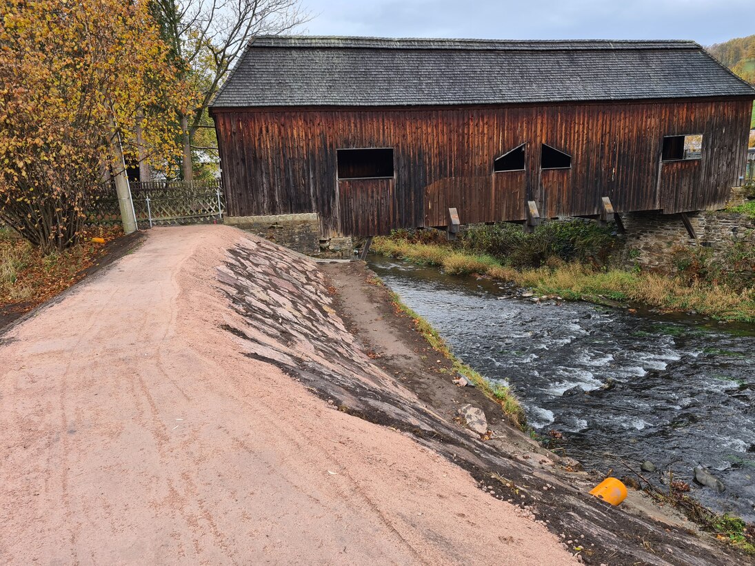 Blick auf alte Scheune, davor ein Weg mit Fluss