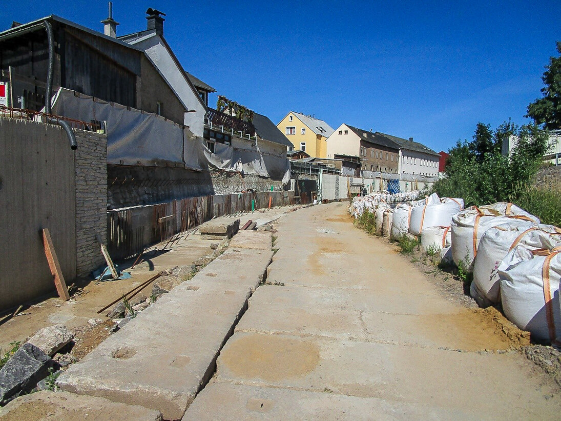Blick auf eine Baustraße mit Betonsteinen, rechts daneben große Sandsäcke, Häuser im Hintergrund