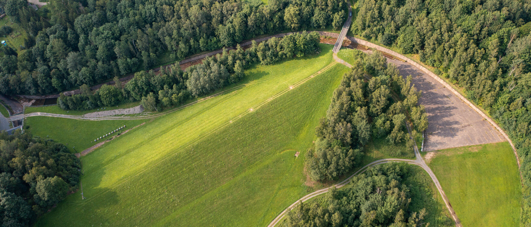 Blick auf den Damm eines grünen Hochwasserrückhaltebeckens