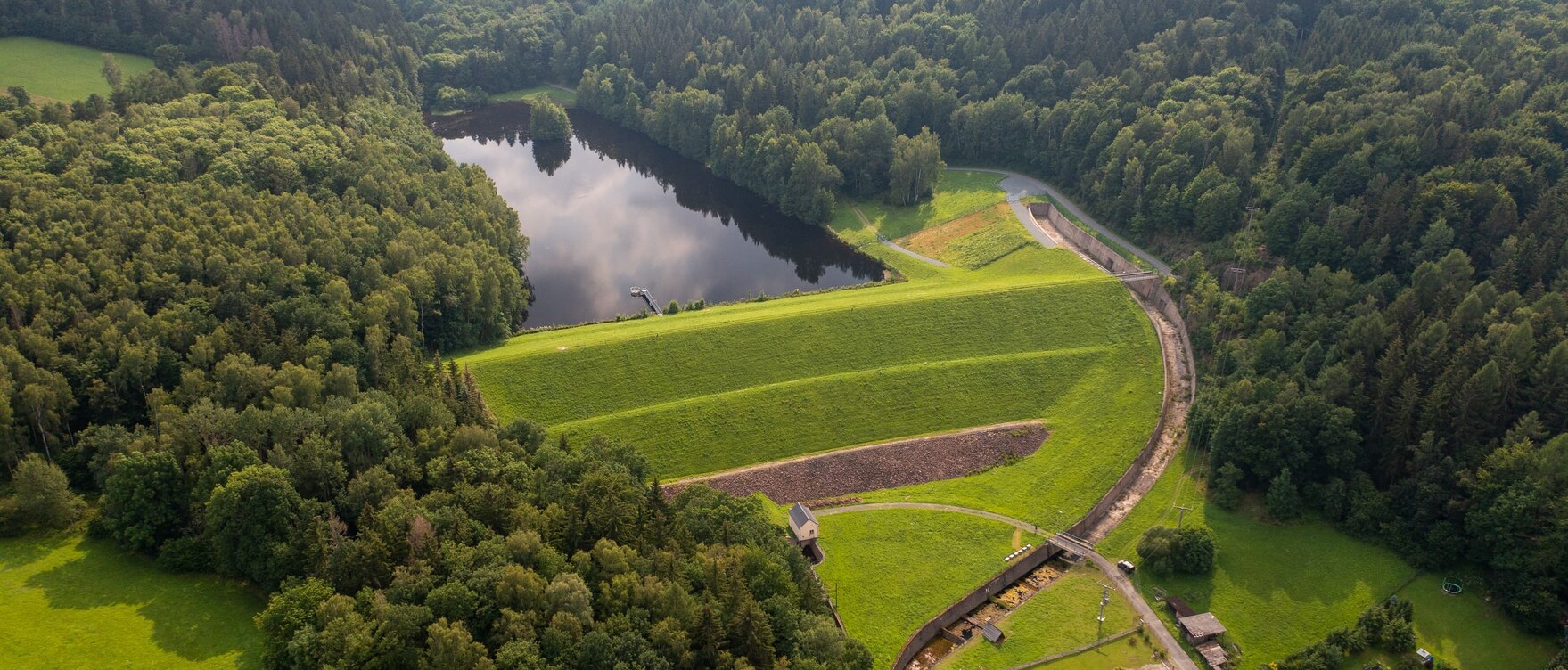 Luftbild vom eingestauten Hochwasserrückhaltebecken umgeben von Wald