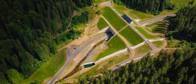 Luftbild eines Hochwasserrückhaltebeckens durch das eine Straße führt