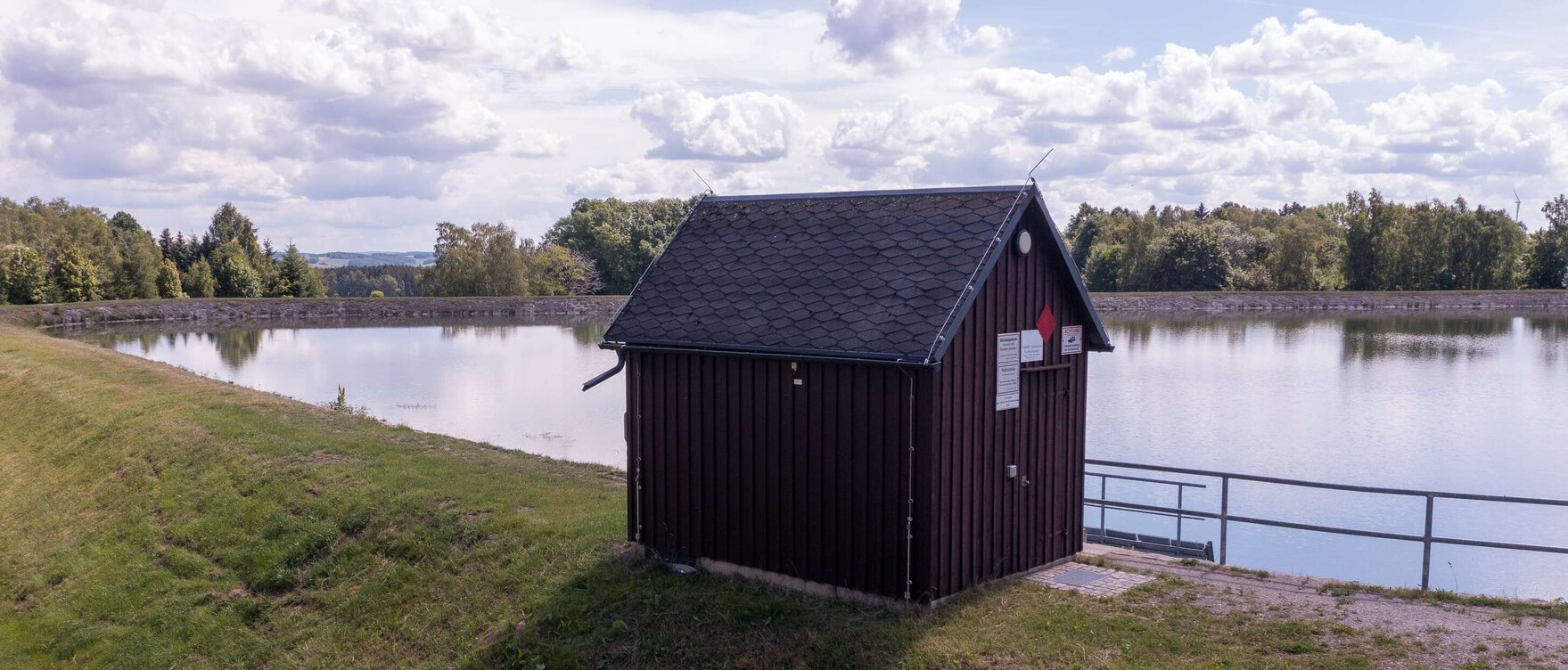Bild eines Sees, an dem ein braunes Holzhaus steht