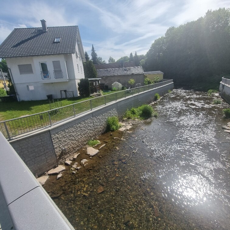 Fluss mit Mauer links und Einfamilienhaus dahinter