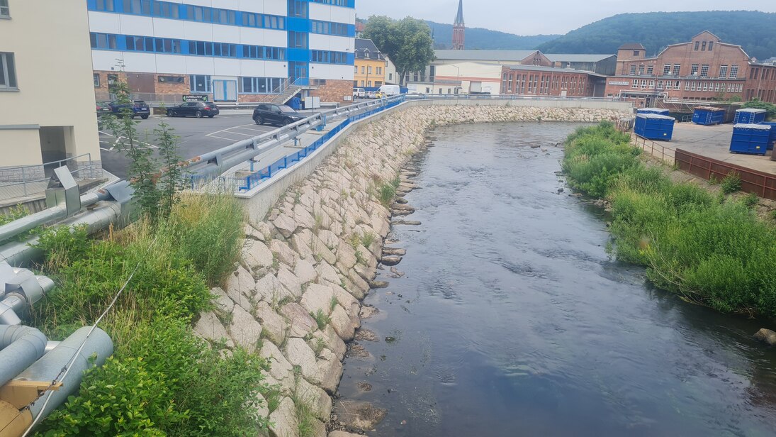 Nahaufnahme vom Fluss mit steinernem Ufer und Bebauung im Hintergrund