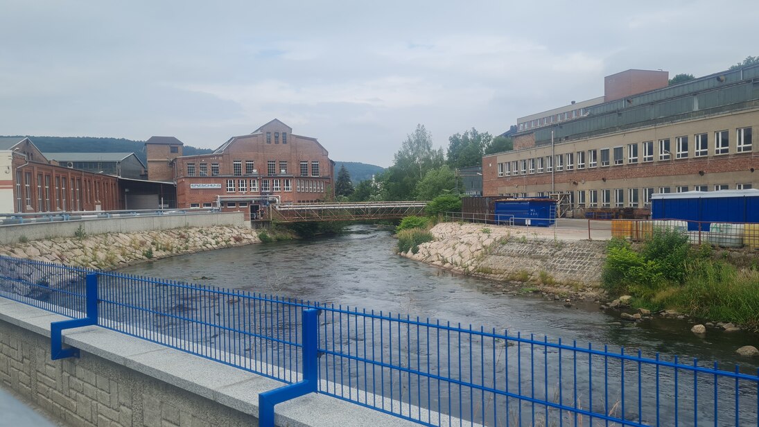 Mauer mit blauem Metallgitter darauf vor einem Fluss