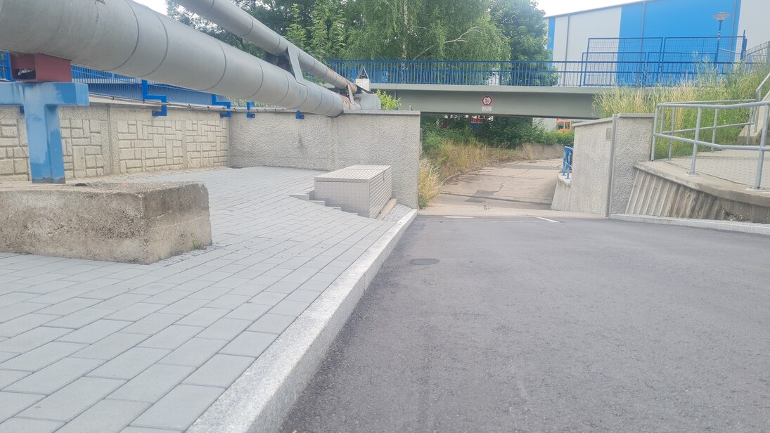 Blick auf dicke graue Rohre die oberirdisch verlaufen, im Hintergrund eine Brücke