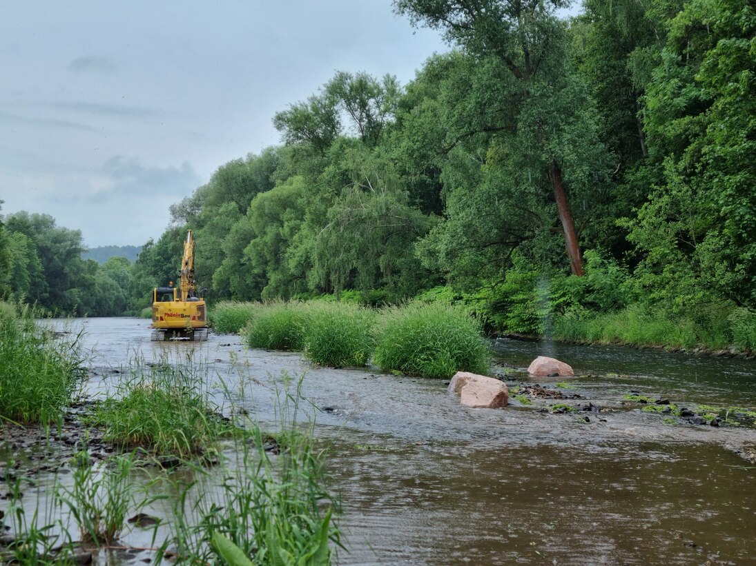 Blick auf einen gelben Bagger im Fluss umgeben von Grün