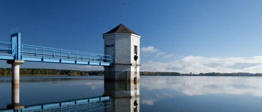 Blick auf einen blauen Metallsteg mit Türmchen am Ende, das in einen See ragt