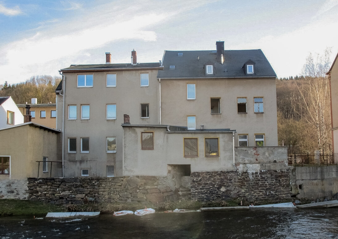 Blick auf ein Doppelhaus mit drei Etagen, das direkt am Fluss steht