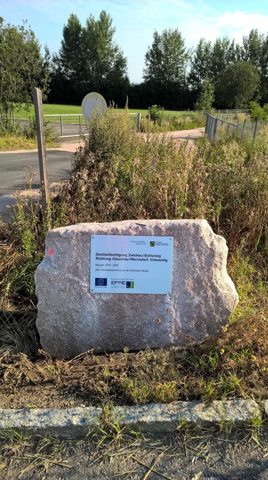 Ein Findling mit einer angebrachten, kleinen Metalltafel steht auf einer Wiese