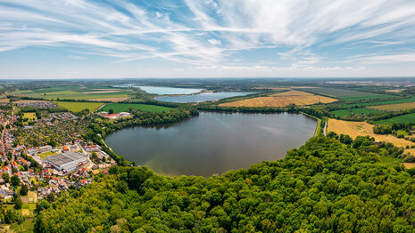 Luftbild des Wasserspeicher Rötha, umgeben von Wald dazu blauer Himmel
