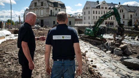 2 Projektleiter der Landestalsperrenverwaltung stehen auf einer Brücke mit dem Rücken zur Kamera und schauen auf die Hochwasserschutzbaustelle in Olbernhau.